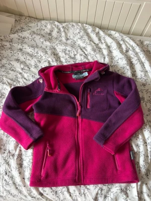 Varm och tjock fleece flickor - OBS!!!  Jag postar bara på helger!!!💛 Denna mysiga fleece till barn har en 3-ficksdesign och är både tjock och varm inuti och utanpå.  Den cerisrosa och lila färgen gör den perfekt för både utomhusaktiviteter och vardagsbruk. Har anpassningsbar luva samt midja. Passar barn 110-130cm långa. Väldigt sparsamt använt inga defekter förutom att dragkedjorna blivit pyttelite gula men inget som påverkat användning och inget som märks. Ev frågor om mått och pris, tveka inte att ställa till mig 💗