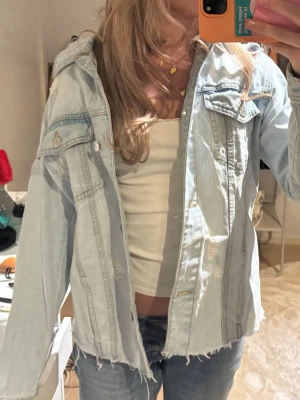 Ljusblå oversized jeansjacka - Säljer en ljusblå oversized jeansjacka med råa kanter och slitna detaljer. Jackan har två bröstfickor med lock och knappar samt klassisk krage. Perfekt för en avslappnad och trendig look.