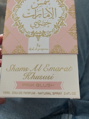 Shams Al Emarat Khususi Pink Blush - Shams Al Emarat Khususi Pink Blush är en parfym i en elegant rosa och vit förpackning med gulddetaljer. Flaskan rymmer 100 ml Eau de Parfum och har en lyxig design som känns både modern och klassisk.