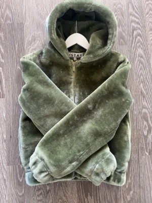 Olivgrön teddyjacka från /STAY🎀 - Supermjuk teddyjacka i olivgrönt från /STAY. Jackan har dragkedja framtill, huva och resår vid ärmslut och midja. 