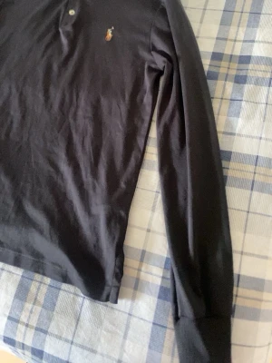 Svart långärmad skjorta från Polo Ralph Lauren - Svart långärmad skjorta från Polo Ralph Lauren med klassisk krage och knappar framtill. Slim fit-modell med broderad logga på bröstet. Tillverkad i mjuk bomull som känns skön mot huden.