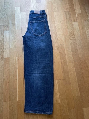 Mörkblå baggy jeans från Zara - Snygga mörkblå jeans från Zara med vida ben och klassisk femficksmodell. Jeansen har kontrastsömmar och en patch bak i midjan. Tillverkade i slitstark denim, perfekta för en trendig och avslappnad look. Midjan 36cm, innerbenslängden 73 cm. Storlek 34.