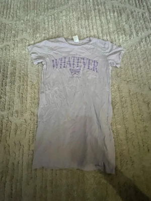 Ljuslila t-shirt med tryck - T-shirt i ljuslila med lila texten 'WHATEVER' och en fjäril på bröstet. Klassisk rund halsringning och korta ärmar. Perfekt för en avslappnad och chill stil.