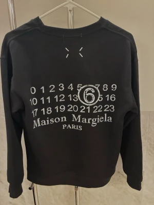 Maison Margiela tröja - Tröjan är i nytt skick och är helt oanvänd. Storleken är XS. Tröjan är svart med vitt tryck där back. Ruggigt fet tröja som passar till nästan allt och är väldigt unik. Pris kan diskuteras. Hör av er vid frågor!