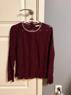 Vinröd spetsblus med lång ärm - Vinröd långärmad blus från Second Female i genombruten spets med fina detaljer. Storlek XS, använd max 4 gånger. 
