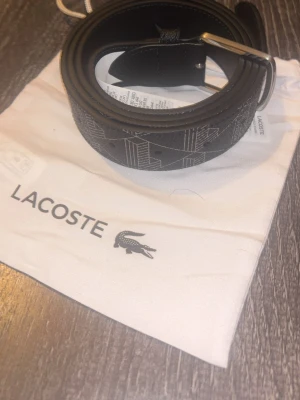Svart bälte från Lacoste med mönster - Säljer nu ett snyggt bälte från Lacoste i läder, säljer det då det var för stort för mig. Det är ej använt. 