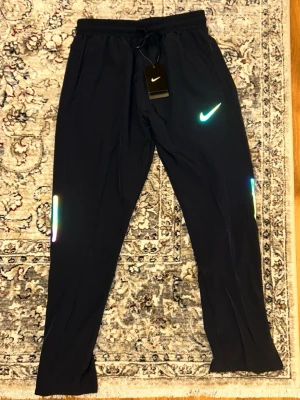 Mörkblå träningsbyxor från Nike - Svarta träningsbyxor från Nike med reflekterande detaljer. Helt nya. Storlek L men sitter som en S/M Skickas inom 48 timmar efter köp🚛