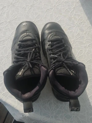 Svarta höga sneakers från Jordan - Snygga svarta höga sneakers från Jordan med klassisk siluett och detaljerad ovandel i läder och textil. Skorna har svarta skosnören, vadderad plös och hälflik med logga. Perfekta för dig som gillar streetwear och sportig stil.