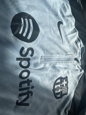 Barça långärmad träningströja Nike - Ljusblå långärmad träningströja från Nike med FC Barcelona-logga och Spotify som sponsortryck. Tröjan har svarta detaljer på axlarna, halv dragkedja framtill och är tillverkad i ett lätt, funktionsmaterial som passar perfekt till träning.                                                                  Storlek: S 📏.                                                             Frakt: Billig och snabb frakt 🚚 💴 (aldrig använd och priset går att diskutera)