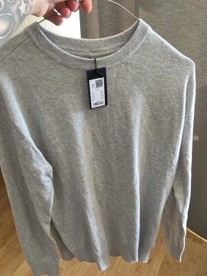 Grå basic sweatshirt från lager - En stilren grå sweatshirt från laget med rund halsringning och ribbade muddar vid ärmslut och nederkant. Perfekt för en avslappnad look och enkel att matcha med andra plagg. Tillverkad i mjuk bomullsblandning.