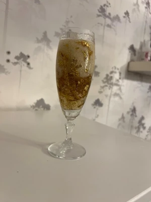 Dekorativt guldig champagne doftljus  - Unikt dekoration doftljus i champagneglas. Perfekt som prydnad eller bordsdekoration. Glaset har elegant fot och smal kupa, och guldflingorna ger en lyxig känsla till inredningen.