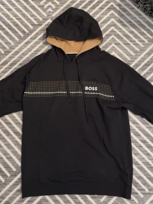 Hugo boss hoodie  - En svart och guldig Hugo boss hoodie som har använts 2 gånger så den är som ny.