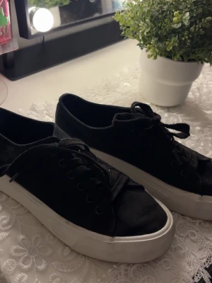 Svarta låga sneakers från Anna Field  - Snygga svarta sneakers från Mansfield med klassisk låg profil och vit tjock sula. Skorna har svarta skosnören och är tillverkade i canvasmaterial som ger en avslappnad vibe. Perfekta för dig som gillar enkel och stilren design.