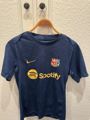FC Barcelona fotbollströja - Snygg blå FC Barcelona matchtröja från Nike med gul logga, klubbmärke och Spotify-sponsor på bröstet. Tillverkad i Dri-FIT-material som andas och har en slim fit-passform. Perfekt för fotbollsträning eller att bära till vardags. Köpt i spanien för 110 Euro