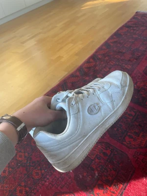 Vita Champion sneakers i läder - Snygga vita sneakers från Champion med klassisk låg siluett. Skorna är gjorda i läder med perforerade detaljer på sidorna och Champion-logga både på sidan och plösen. Perfekta för en clean och sportig look.