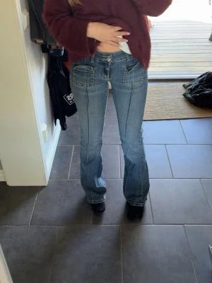 Blå bootcut jeans med fickor fram - Snygga blå bootcut jeans med markerade sömmar och två stora fickor framtill. Jeansen har en klassisk femficksdesign och är tillverkade i denim med lätt stretch. Perfekta för en avslappnad och trendig look.