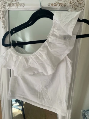 Trendig vit one shoulder volang topp - Trendig vit one shoulder volang topp. Helt ny inte använd en ända gång, säljer då den inte kommer till användning. Tryck gärna på köp nu!