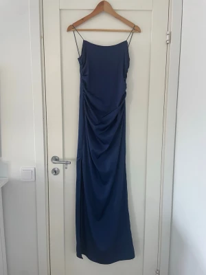 Mörkblå balklänning med tunna band - Elegant mörkblå balklänning med tunna axelband. Klänningen har en rak, smickrande siluett och är tillverkad i ett mjukt, glansigt material som ger en lyxig känsla. Perfekt för dig som vill ha en stilren och modern look. Endast använda en gång☺️💐🫐Uppsydd för mig som är 169