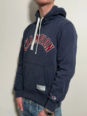 Mörkblå Champion hoodie med huva - Mörkblå hoodie från Champion med ett simpelt men snyggt tryck. Tröjan är size S skick8/10. Passar perfekt nu till våren!! Modellen är 176cm lång väger 65kg.MVH zen_market