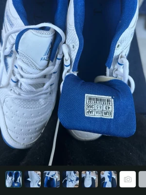 Vita och blå sneakers Fashion - Snygga vita sneakers med blå detaljer från Fashion. Skorna har låga skaft, perforerade partier och klassisk snörning. Tillverkade i syntetmaterial med sportig design och bekväm passform. Perfekta för en stilren vardagslook.