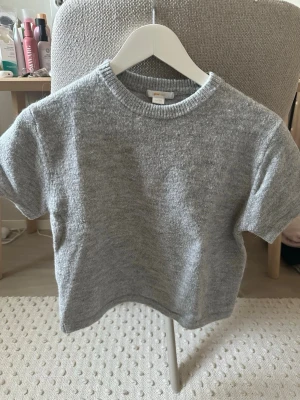 Grå stickad kortärmad topp - Mysig grå stickad topp med korta ärmar och rund hals. Perfekt för lager på lager och enkel att matcha med olika stilar. Mjuk och skön känsla, passar både till jeans och kjol.