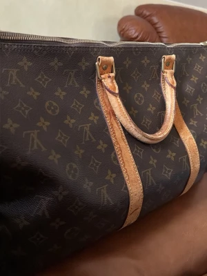 Louis Vuitton monogram resväska - Säljer en klassisk Louis Vuitton resväska i brunt canvasmaterial med ikoniskt monogrammönster och detaljer i ljust läder. Väskan har dubbla handtag och robust dragkedja i metall. Perfekt för dig som vill resa med stil. Väskan är sliten vid handtagen och har några fläckar på insidan fast går bort med lite sprit. Annars är den genuin och är väldigt vintage.