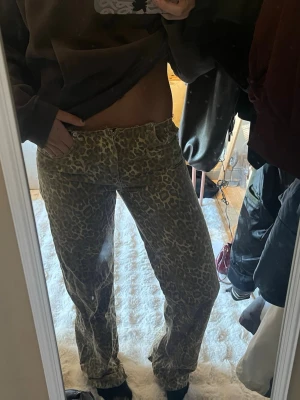 Leopardmönstrade jeans med raka ben - Säljer ett par coola leopardmönstrade jeans med raka ben och klassisk femficksdesign. Jeansen har en beige och brun färgkombination och är tillverkade i ett denim-material. 