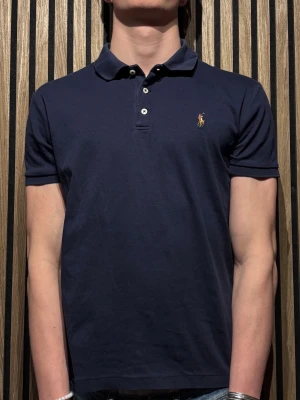 Mörkblå pikétröja från Ralph Lauren - Klassisk mörkblå pikétröja från Ralph Lauren. Storlek L men den är liten i storleken så den passar även M