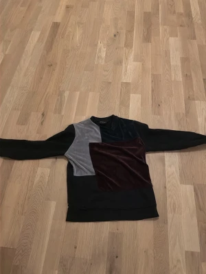 La vichy  - Unik långärmad tröja från Vichy i sammet med patchwork-design i svart, mörkblått, vinrött och grått. Tröjan har rund halsringning och en oversized känsla. Perfekt för dig som gillar statement-plagg och mjuka material.