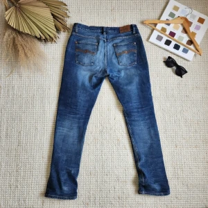 Nudie jeans Lean Dean W33 L34 🔥 - Klassiska blå jeans från Nudie Jeans med den ikoniska orangea "M"-läderlappen bak, gul-orange sömmar och snygg wash. Slim/straight fit som sitter bra. Storlek: W33 L34 – sitter som normal herrstorlek. Skick: Mycket bra skick – har använts sparsamt. Det finns ganska stora hål på insidan av båda framfickorna. Hålen syns inte när man har byxorna på sig, men de gör att fickorna inte fungerar bra om man vill förvara saker i dem. Rekommenderar därför inte det. Annars inga andra defekter eller slitage.
