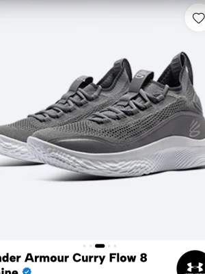 Grå Under Armour Curry Flow 8 - Snygga grå sneakers från Under Armour, modell Curry Flow 8. Skorna har en stickad ovandel i mesh för bra andningsförmåga, vita vågiga sulor och diskret logga på sidan. Perfekta för dig som gillar sportig och modern stil. Storlek 45, höger sko lite skadad på baksida se näst sista bild