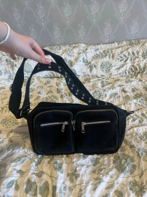 Noella Celina bag - Jätte fin axelremsväska från Noella i modellen Celina. Säljer den då den inte längre används.  Mycket förvaringsplats med 6 småa fack och 1 stort, alla fack har dragkedja förutom 1 inuti. 2st band - 1 längre med platta nitar och 1 längre justerbart vilket ger en valmöjligheter. Den är svart med silvriga detaljer. 🌸