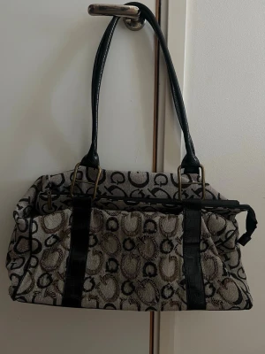 Stor vintage väska! - Snygg handväska  med klassiskt monogrammönster i svart och guld på beige bakgrund. Väskan har svarta handtag och detaljer i fejkläder med krokopräglad struktur samt guldfärgade metalldelar. Perfekt för dig som gillar statement-accessoarer. (Väskan är i fint skick , se dock bild 2 där det finns några trådar, endast de jag kan hitta som defekt)