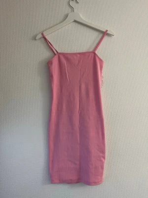 Rosa ribbad klänning från Amisu - Säljer en rosa ribbad klänning från Amisu i storlek EU 34. Klänningen har smala axelband och en kroppsnära passform som ger en snygg siluett. Perfekt för dig som gillar en enkel men trendig look.