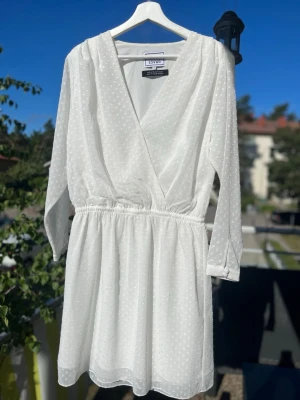 Vit omlottklänning Grace - Söt vit kortklänning, omlott framtill och resår i midjan. Klänningen har långärmade ärmar och lätt v-ringad hals. Perfekt för sommarens alla tillfällen! Skickas eller hämtas Hägerstensåsen. 🤍