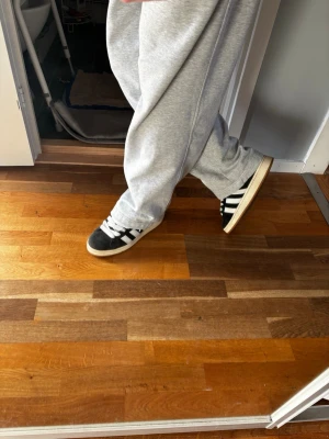 Adidas campus 00s storlek 44 - Klassiska svarta Adidas sneakers med vita ränder och breda vita skosnören. Skorna har låg profil och en beige sula. Ovandelen är i mocka och textil, med Adidas logga på plösen. Perfekta för en avslappnad streetwear-look. Skick: nästintill perfekt, ändå tecknen på användning är lite smuts men går att tvätta bort. Fråga gärna om du har funderingar🤍