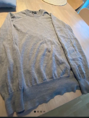 Ljusgrå stickad tröja Tiger of Sweden - Ljusgrå stickad tröja från Tiger of Sweden med rund halsringning och långa ärmar. Tröjan har en enkel och stilren design, perfekt för lager på lager. Materialet ser mjukt och tunt ut, vilket gör den skön att bära.