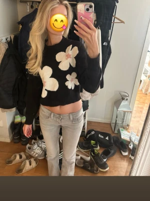 Svart cropped stickad tröja med blommor - Säljer en svart cropped stickad tröja med stora vita och ljusrosa blommor på framsidan. Från H&M i storlek S. Tröjan har långa ärmar och en avslappnad passform. Perfekt för dig som gillar trendiga och lekfulla plagg.