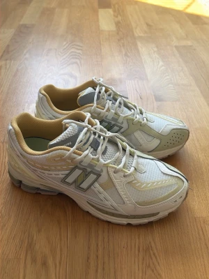 Beige New Balance sneakers - Snygga beige sneakers från New Balance med mesh och syntetpaneler, beige detaljer och klassisk N-logga på sidan. Skorna har vita snören, ventilerande ovandel och en chunky sula som ger retrovibbar. Perfekta för dig som gillar sportig stil.