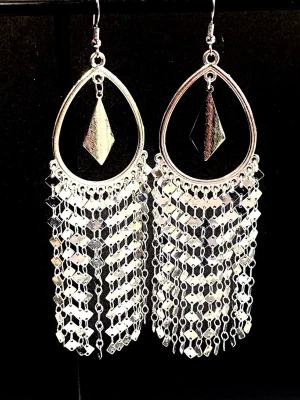 Långa platinum örhämgen med länk-kedjor  - Säljer ett par stora silvriga örhängen med droppformad ram och hängande fransar av små, blanka metallbrickor. Örhängena har även en diamantformad detalj i mitten. Perfekta för dig som gillar att sticka ut med accessoarer. Längd 14cm 