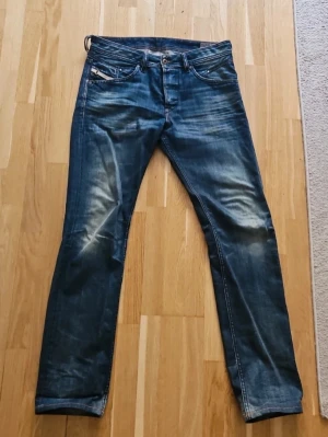 Diesel - Belther - Säljer ett par blå slim fit jeans från Diesel med snygg slitning och klassisk femficksmodell. Jeansen har en något tvättad look och raka ben. Tillverkade i bomull med detaljer i kontrastsömmar och läderpatch bak i midjan.