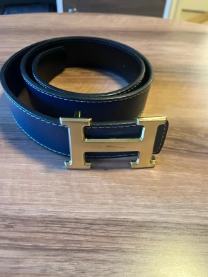 H spänne bälte - Längd 105cm använd därav priset. Guld spänne färg marinblå navy.