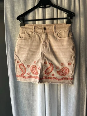 Korallfärgad jeanskjol - Säljer en beige/korall färgad kjol med paisleybrodyr längs nederkanten. Knappt använd