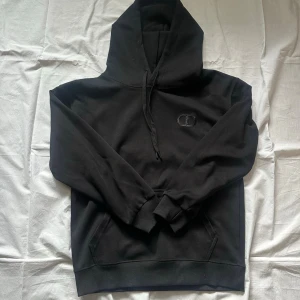 Svart hoodie  - Säljer en svart hoodie  med broderad logga på bröstet. Hoodien har klassisk huva med dragsko, känguruficka framtill och ribbade muddar vid ärmar och nederkant. Perfekt för en stilren och avslappnad look.