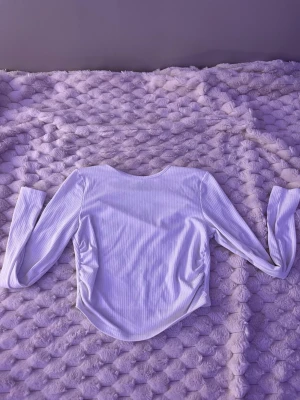 Vit ribbad långärmad topp - Säljer en vit ribbad långärmad topp med figurnära passform och lätt rundad nederkant. Toppen har diskreta rynkdetaljer i sidorna som ger en snygg siluett. Perfekt att styla med jeans eller kjol.