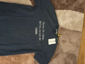 Blå Acne Studios t-shirt - Snygg mörkblå t-shirt från Acne Studios med tryck 'Acne Studios STOCKHOLM 1996' på framsidan. Klassisk rund hals och korta ärmar. Perfekt för dig som gillar stilrena plagg med en modern touch.