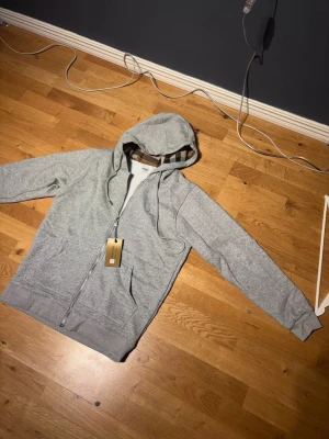 Grå zip hoodie från Burberry - Snygg grå hoodie från Burberry med dragkedja, snygg hoddie, aldrig använd, perfekt för kyliga sommarkvällar! Eller till dig som vill ha en stilren och snygg look! Tveka ej på frågor eller funderingar😀