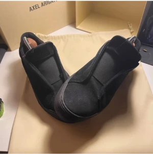 Svarta sneakers från Axel Arigato - Stilrena svarta sneakers från Axel Arigato i mocka med minimalistisk design. Skorna har en låg silhuett, svart sula och diskret logga på sidan. Litet hål i båda skona.