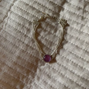 Silverfärgat armband med lila sten från LBVYR - Snyggt silverfärgadt armband från LBVYR med en lila sten i mitten. Armbandet har en justerbar kedja och flera tunna länkar som ger en elegant look. Perfekt för att piffa upp vilken outfit som helst! 💜