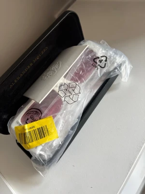 Vita solglasögon Alexander McQueen - Snygga solglasögon från Alexander McQueen med vita, rektangulära bågar och rosa glas. Kommer i originalfodral. Perfekta för dig som vill sticka ut med en cool och modern look.